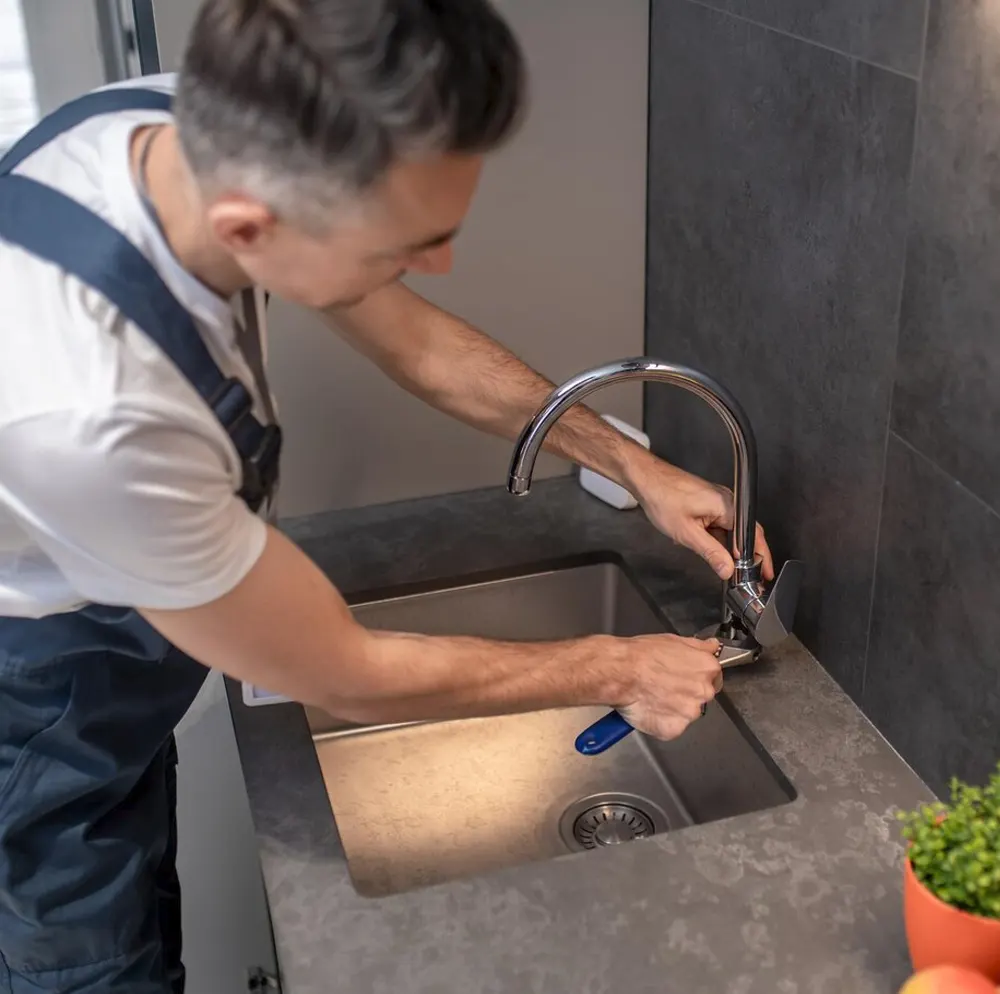 A professional plumber in Jersey using a wrench to fix a blocked kitchen sink tap.