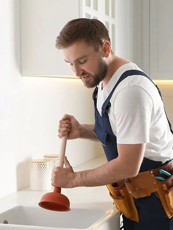 An expert plumber using a plunger to clear a clogged kitchen sink in Jersey,