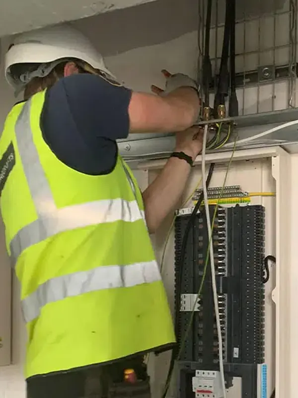 A local electrician in Jersey wearing NICEIC-approved uniform of high-visibility vest and hard hat.