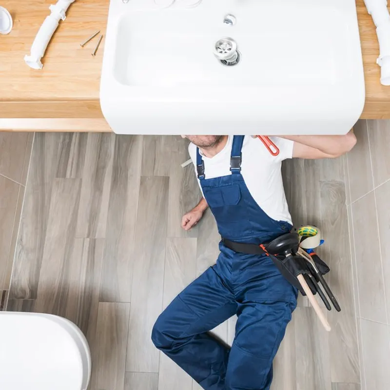 A professional plumber in Jersey inspecting and fixing a bathroom sink for potential leaks.