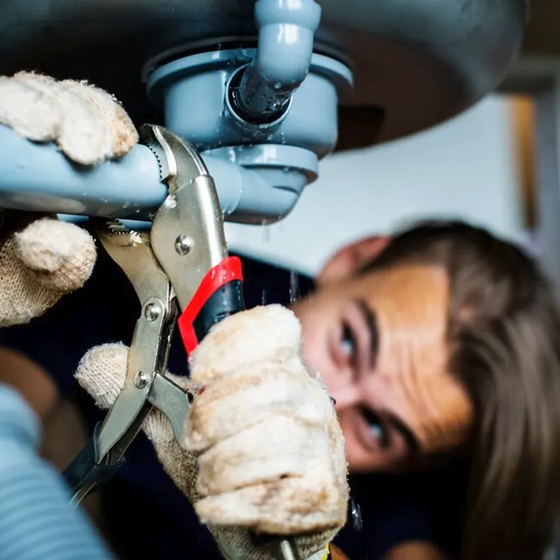 A Jersey plumber using a wrench to fix a leaking pipe under a sink.