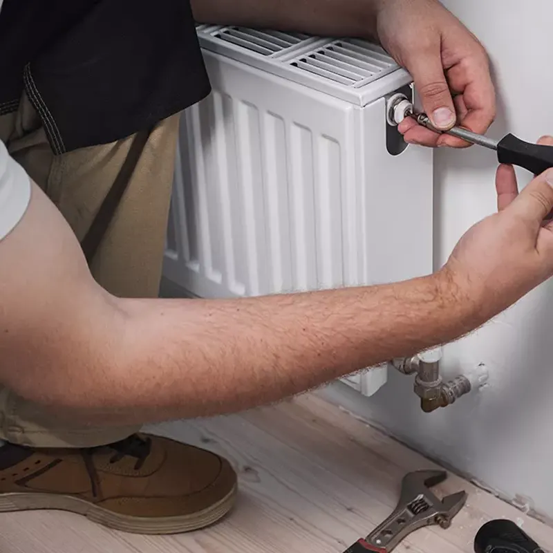 A professional heating engineer using a screwdriver to install or repair a central heating radiator in Jersey.