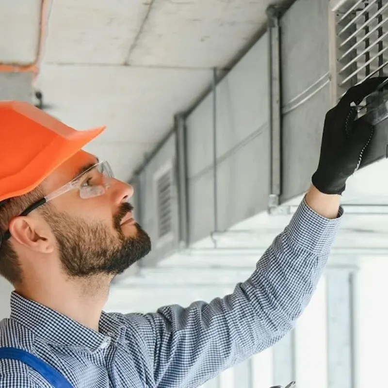 A professional heating engineer in safety gear inspecting a commercial ventilation system in a Jersey industrial building.